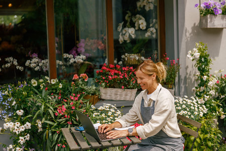 Beautiful flower shop owner wearing apron working on laptop in her store
