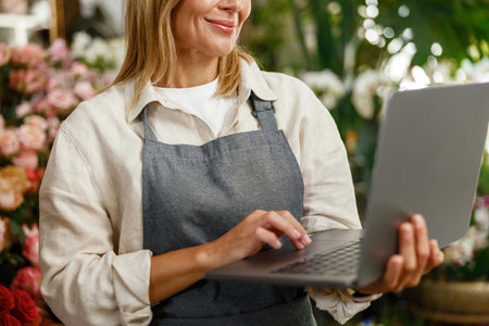 Close up of florist wearing apron working on laptop and taking online orders in storeの写真素材