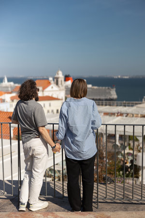 Back view of romantic hipster couple in love holding hands while walking on old city streetの写真素材