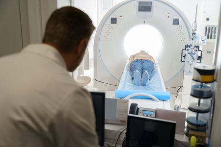 Doctor radiologist controls MRI or CT or PET Scan with female patient undergoing procedureの写真素材