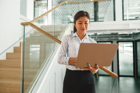 Smiling woman sales manager working on laptop while standing on stairs in coworking backgroundの写真素材
