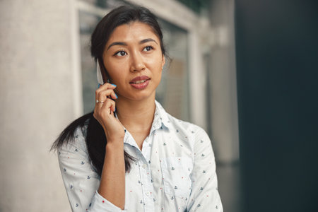 Woman entrepreneur talking phone with client while standing in office and looking at side