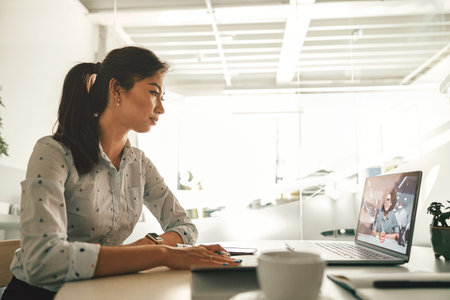 Businesswoman during online video conference with colleague while sitting in officeの写真素材