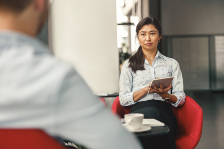 Female HR manager holding digital tablet and looking on job candidate during an interviewの写真素材