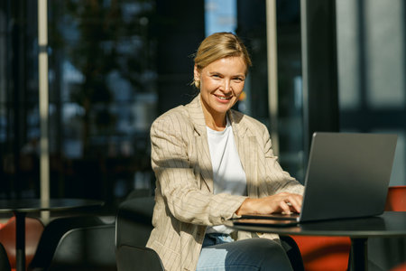 Smiling female entrepreneur working on laptop in modern office hall and looks cameraの写真素材
