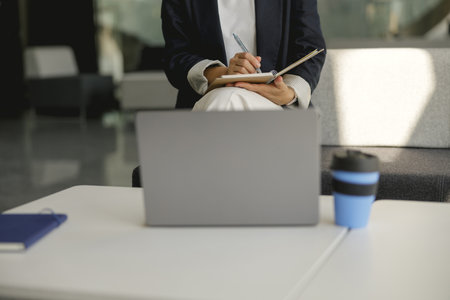 Close up of business woman is making notes during work on laptop in officeの写真素材