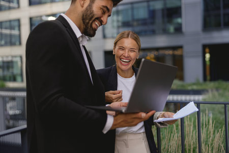 Smiling business colleagues discuss biz issue while use laptop standing on office terraceの写真素材