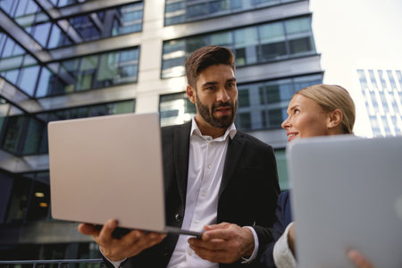 Smiling business colleagues discuss biz issue while use laptop standing on office terraceの写真素材