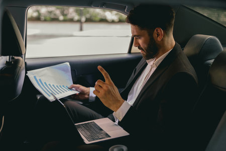 Confidence businessman sitting on car backseat and working with documents and use laptop
