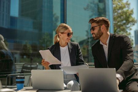Business colleagues working with documents and use laptop sitting outside of office on cafe terrace