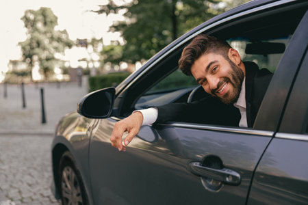 Smiling male driver in suit is riding behind steering wheel of car and looks cameraの写真素材
