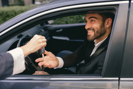 Close up of smiling business man in suit receiving car keys to new vehicleの写真素材