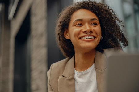 Close up of smiling female manager working on laptop while sitting in cafe terrace and looks away