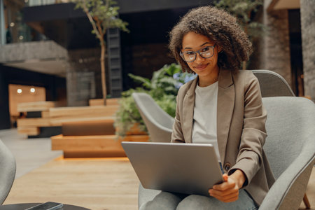 Smiling businesswoman working on laptop while sitting in modern coworkingの写真素材