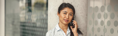 Smiling female freelancer talking phone with client while standing in coworking and looking camera