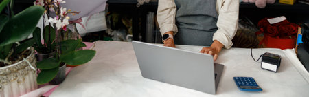 Beautiful flower shop owner wearing apron working on laptop in her storeの写真素材