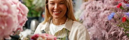 Smiling woman flower shop owner in apron looking on bouquet of flowers at florist storeの写真素材
