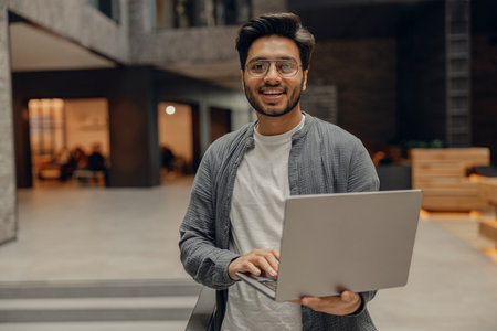 Smiling freelancer in eyeglasses with laptop standing on modern coworking backgroundの写真素材