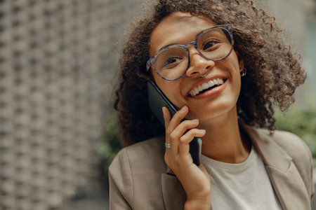 Smiling businesswoman is talking phone with client while standing on office background