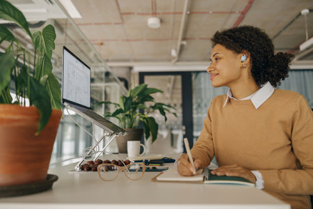 Smiling woman architect designer working on project while use laptop and making notes in office
