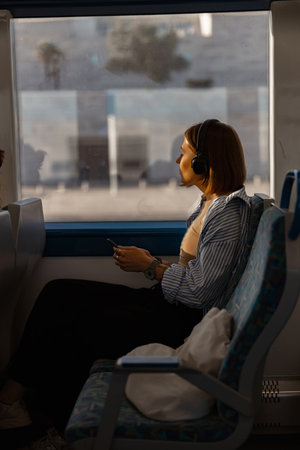 Woman in headphones while traveling in public transport and looking view outside the windowの写真素材