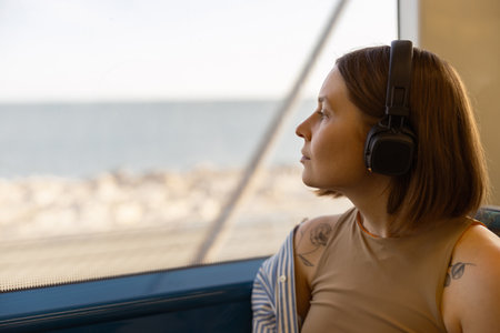 Woman in headphones while traveling in public transport and looking view outside the windowの写真素材