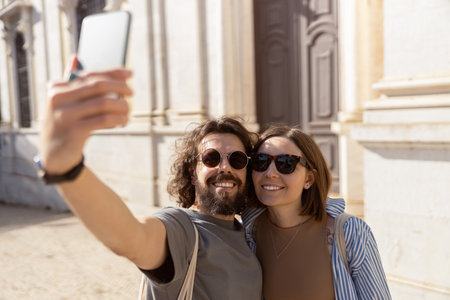 Smiling tourist couple walking in city street and making selfie on phoneの写真素材