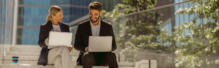 Two business colleagues working on project while sitting outdoors on skyscrapers background