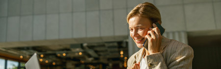 Smiling businesswoman talking on phone with client while working on laptop in office