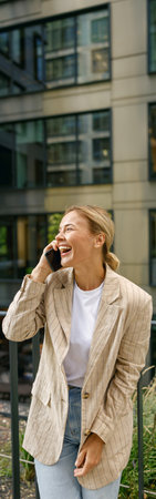 Businesswoman talking phone whiile standing on modern building background and looking at side