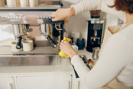 Close up of female barista cleaning coffee machine at coffee shop after froths milkの写真素材