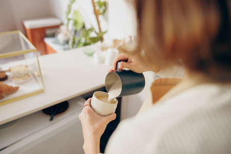 Back view of female barista makes coffee and pours it into a mug while working in coffee shopの写真素材