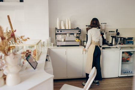 Back view of female barista grinding coffee using professional grinder machine in coffee house