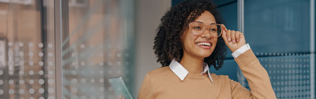 Smiling businesswoman holding phone while standing on modern office background and looks awayの写真素材