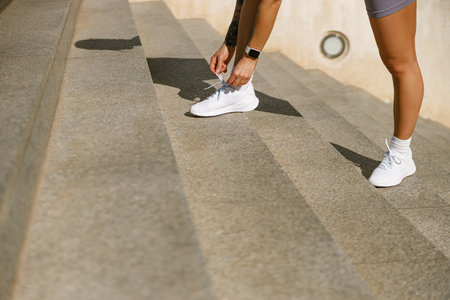 Close up of sporty woman tying shoelace on running shoes before practice outdoors