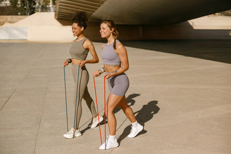 Two fitness women doing exercise with resistance elastic band outside in urban environment