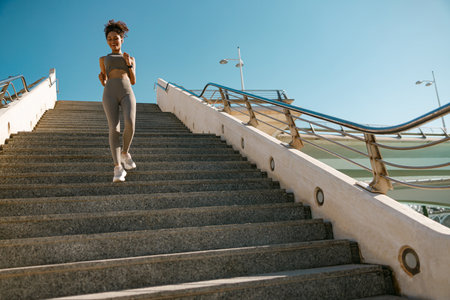 Active female athlete in sportswear running on steps outdoors on a sunny day. Reaching the goalの写真素材