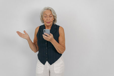 An Elderly Woman Actively Engaging with Her Smartphone in a WellLit Studio Environmentの写真素材