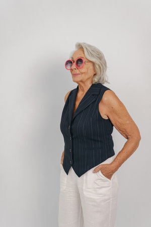A stylish senior woman wears a vintage vest and trendy sunglasses, exuding confidence