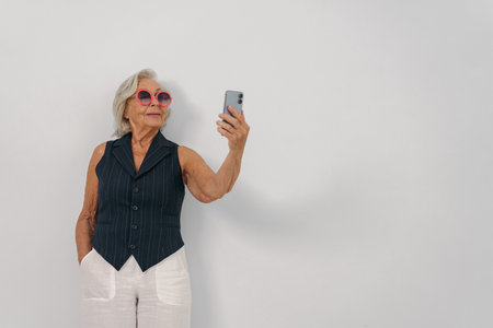 A confident and stylish senior woman is happily taking a selfie with her modern smartphone