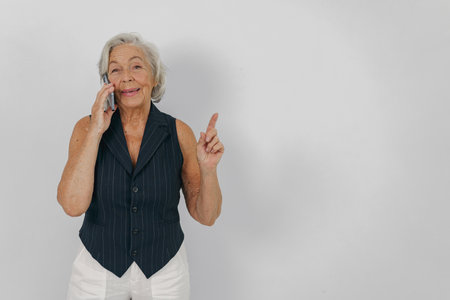 An Elderly Woman Engaging in a Phone Conversation, Displaying a Positive Gesture Enthusiasticallyの写真素材