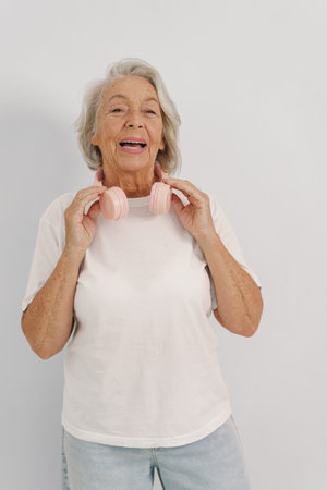 A Joyful Elderly Woman Wearing Headphones Poses Against a Simple, Plain Backgroundの写真素材