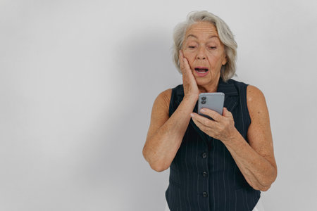 A Surprised Elderly Woman Enthusiastically Using Her Smartphone, Embracing Modern Technologyの写真素材