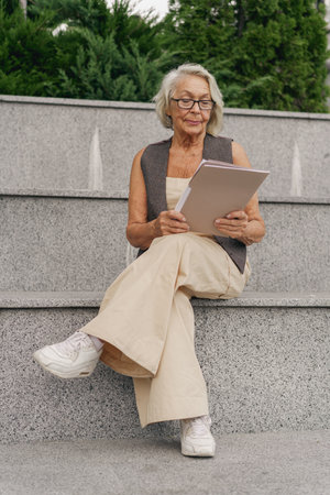 An Elegant Senior Woman Enjoying Reading a Book in a Peaceful Outdoor Spaceの写真素材