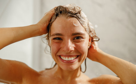 A cheerful woman joyfully enjoying a refreshing shower while lathering her hair with shampooの写真素材