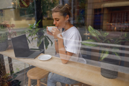 Woman Enjoying Coffee While Working on Laptop in Cozy Caf