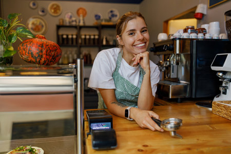 A friendly barista with a warm smile greets customers, enhancing the cozy coffee shopの写真素材