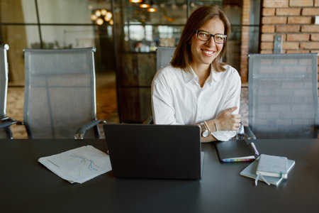 A Professional Office Worker with a Bright Smile While Sitting at Their Desk Using a Laptopの写真素材
