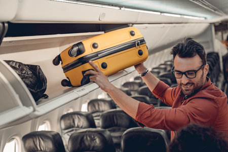 A Passenger Carefully Loading Their Luggage Into the Airplanes Overhead Storage Binの写真素材