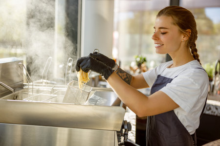 A Chef Engaged in Cooking Within a Busy Restaurant Kitchen Utilizing a Fryer for Dishesの写真素材